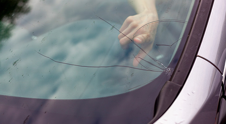 Closeup of a finger pointing at a cracked windshield