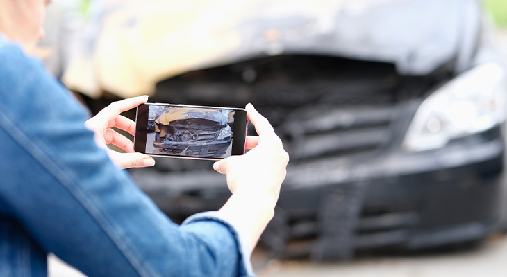 Closeup of a woman photographing damaged car