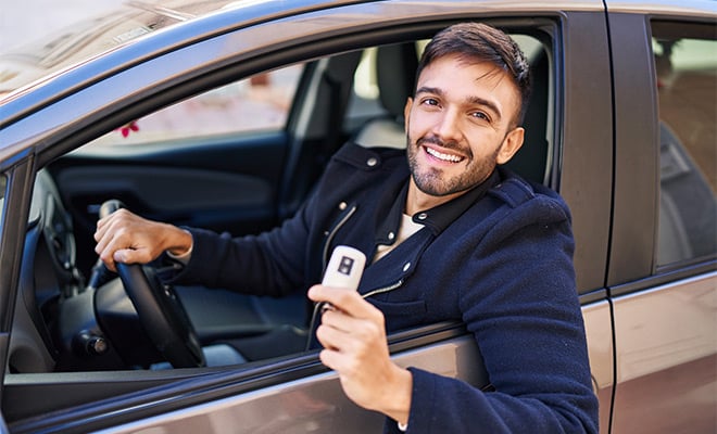 Young man smiling and holding keys by the car window