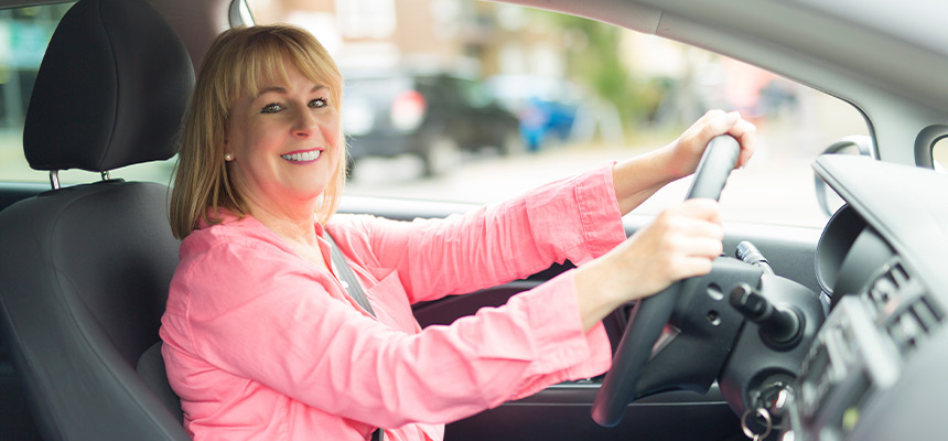 White woman wearing pink driving and smiling