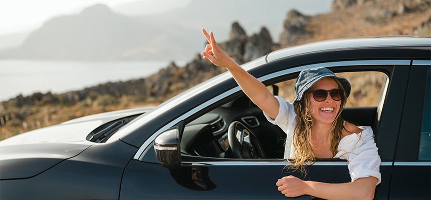 Young woman with sunglasses doing a peace sign by window of car