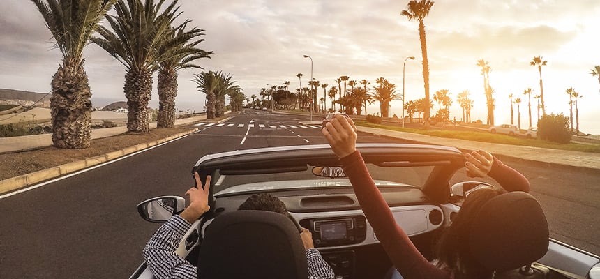 Couple driving convertible car in street surrounded with palm trees