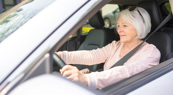 Senior woman wearing pink sweater driving car