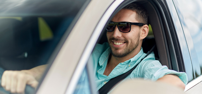 Young smiling man wearing sunglasses while driving