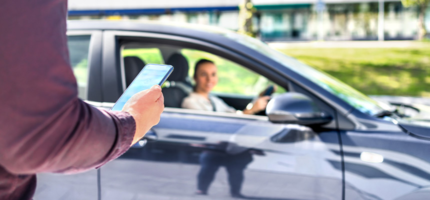 Man using phone for rideshare with driver waiting in the distance