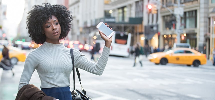 Young Black woman waiting for her rideshare and holding her phone